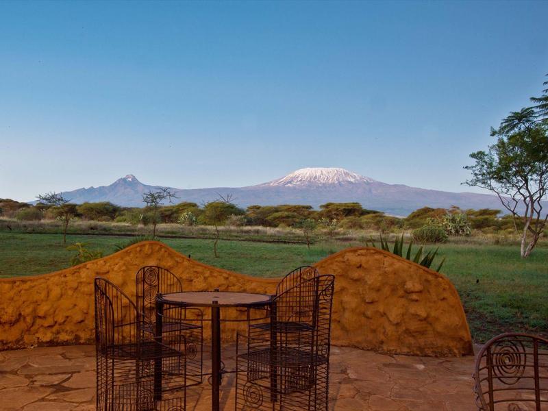 Vista desde una terraza con sillas hacia un paisaje verde y montañas nevadas al fondo.