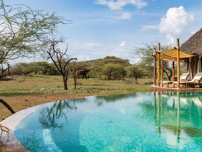 Infinity-Pool neben Safari-Lodge mit Blick auf offene Savanne und Akazienbäume.