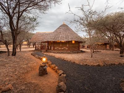 Ein rustikales Ferienhaus aus Holz mit Strohdach umgeben von Bäumen und einem Weg bei Dämmerung.