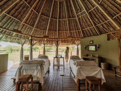 Offener, strohgedeckter Wellnessbereich mit Massageliegen und Holzmöbeln in natürlicher Umgebung.