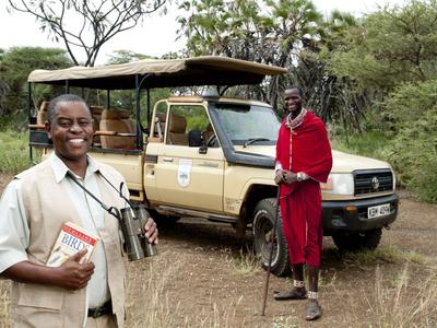 Zwei Personen in Safari-Kleidung vor einem Jeep in einer Savannenlandschaft.
