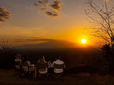 Vier Personen sitzen draußen und beobachten einen orangefarbenen Sonnenuntergang über der Landschaft.