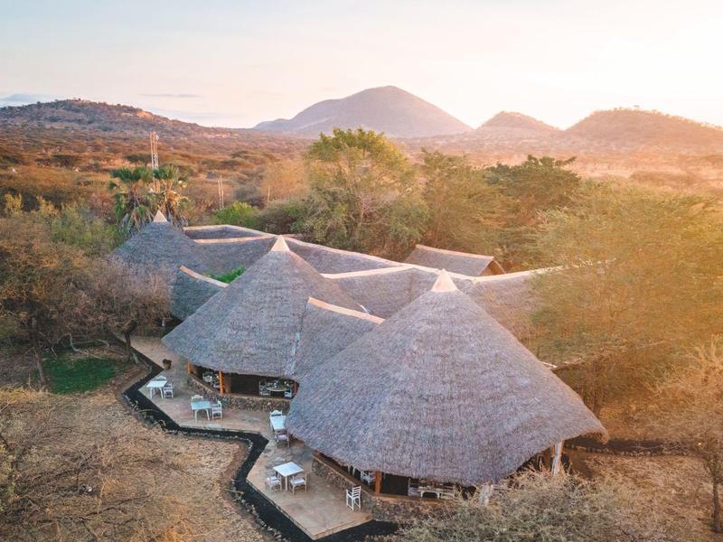 Vue d'ensemble d'un complexe tropical avec des bungalows au toit de chaume dans un paysage ensoleillé.