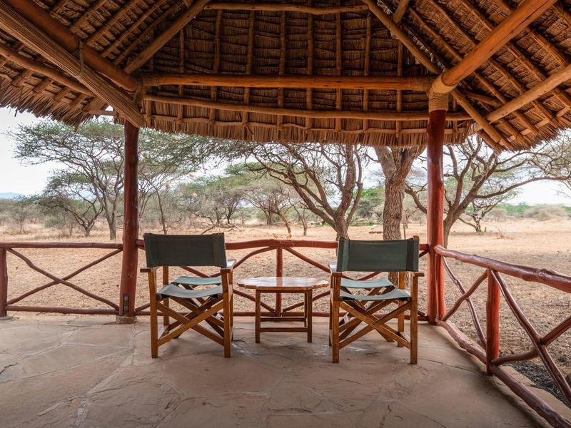 Terrasse couverte avec deux chaises et une table face à la savane sèche et arbres d'acacia.