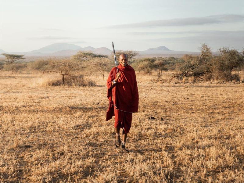 Homme en robe rouge marchant dans une savane sèche.