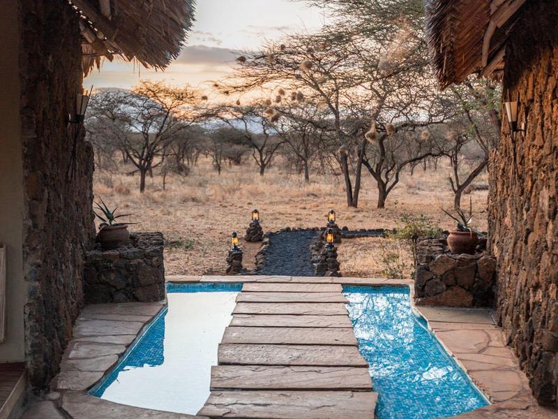 Piscine entourée de cabanes en pierre avec vue sur la savane au coucher du soleil.