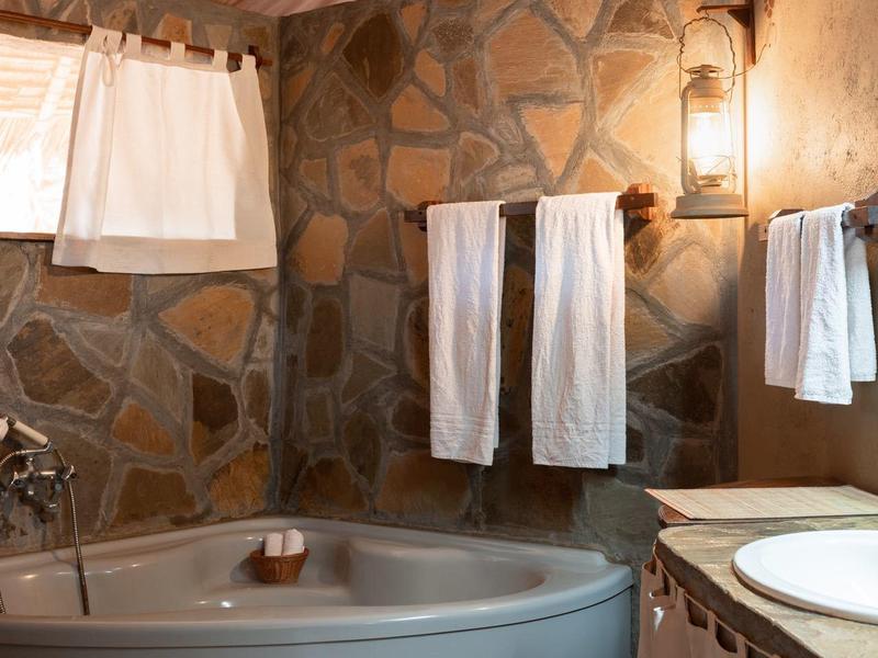 Salle de bain confortable avec baignoire d'angle, mur en pierre et serviettes blanches.