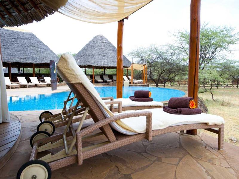 Chaise longue sur terrasse avec vue sur piscine et savane africaine en arrière-plan.