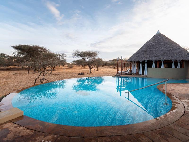 Piscine à l'eau claire à côté d'un bâtiment rond au toit de chaume dans un paysage sec.