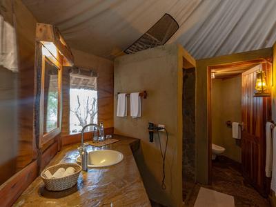 Rustikales Badezimmer mit Holz und Zeltstoff, Waschbecken und separater Dusche in einer Lodge.