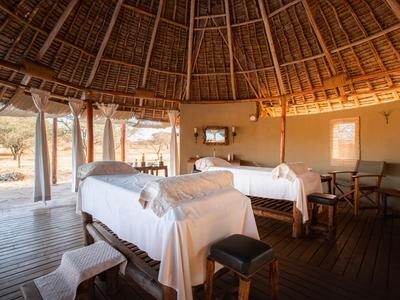 Innenraum einer offenen Lodge mit zwei Massageliegen, Holzdach und Blick nach draußen.