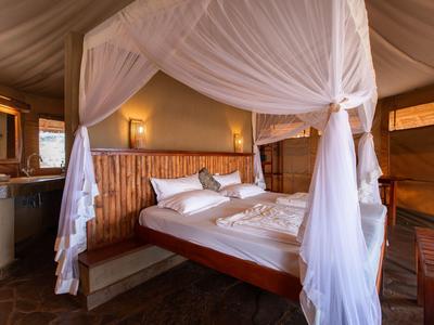 Gemütliches Bett mit Moskitonetz in einem luxuriösen Zelthotelzimmer mit Holzdekor.