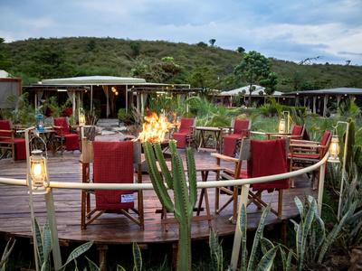 Round wooden deck with seats, torches, and lamps, surrounded by green vegetation.