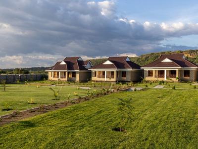 Three small houses with brown roofs on a vast green field under a cloudy sky.