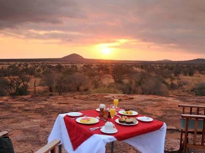 A set table with red cloth and dishes overlooking a landscape at sunset.