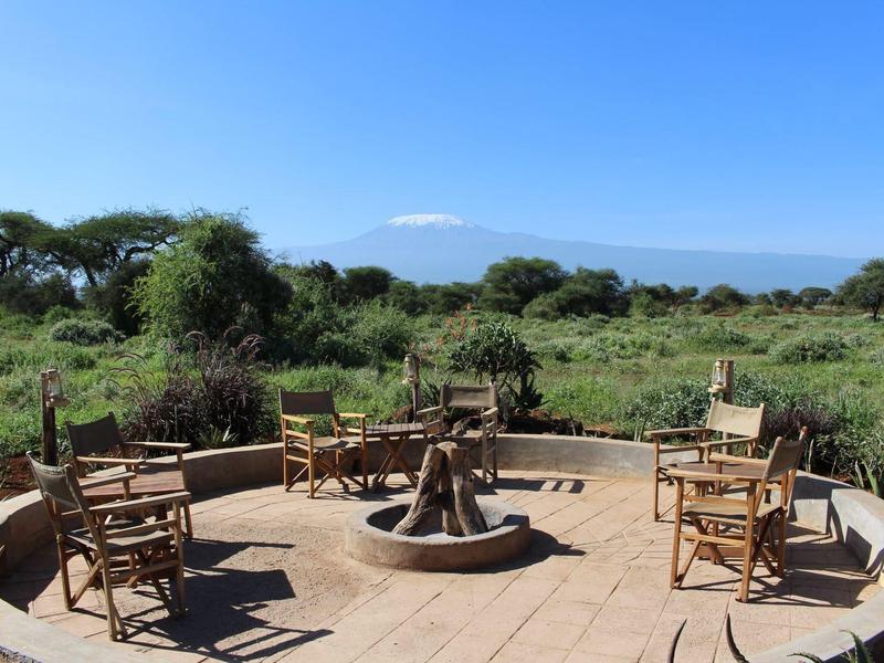 Outdoor fire pit area with chairs overlooking green landscape and mountain in the background.