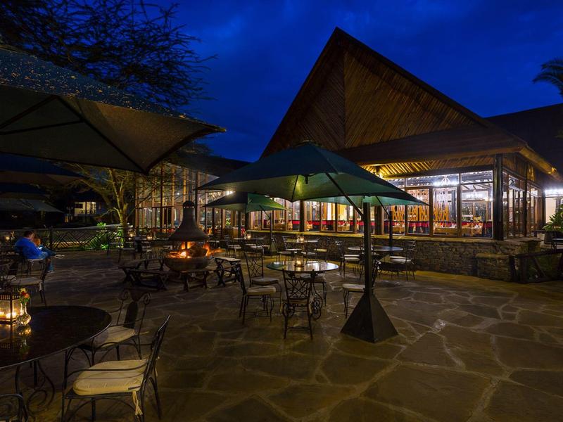Hotel terrace at night with tables, chairs, and illuminated indoor area.