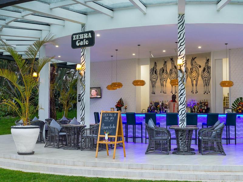 Modern outdoor bar area with tables, chairs, and illuminated counter next to palm decor.