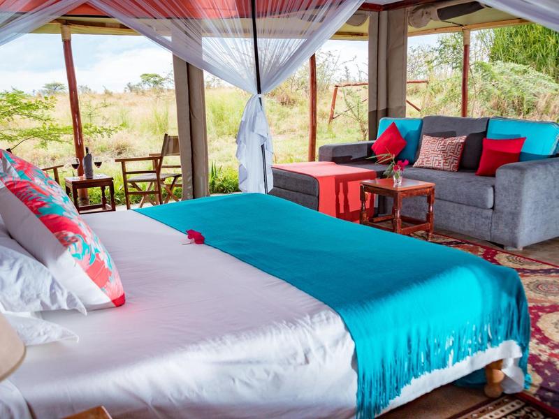 An open room with a cozy bed, sofas, and a view of natural surroundings.