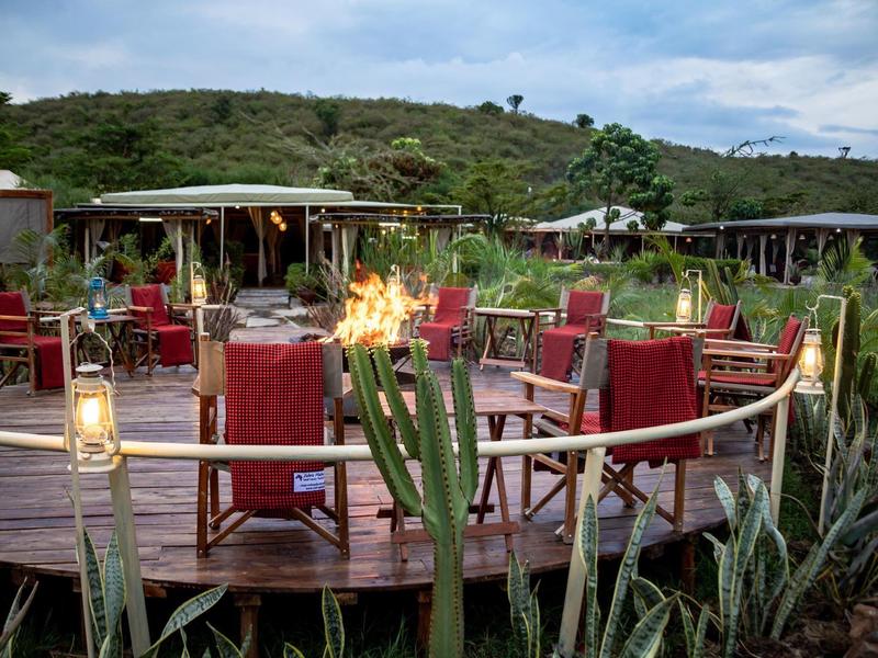 Round wooden deck with seats, torches, and lamps, surrounded by green vegetation.