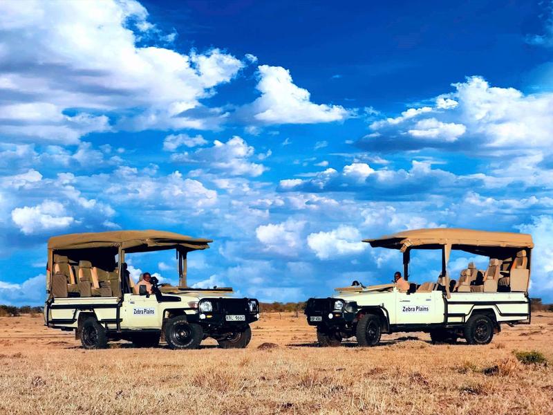 Two jeeps with passengers face each other on a dry savanna under a blue sky.