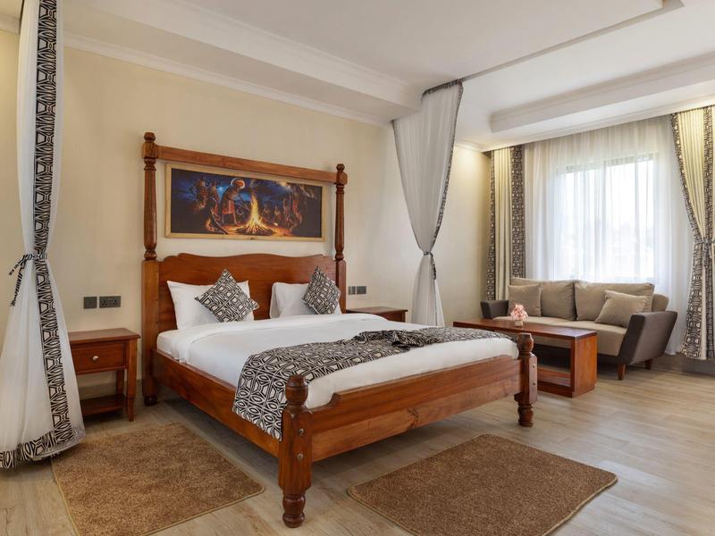 Elegant hotel room with wooden bed, sofa, and large windows for daylight.