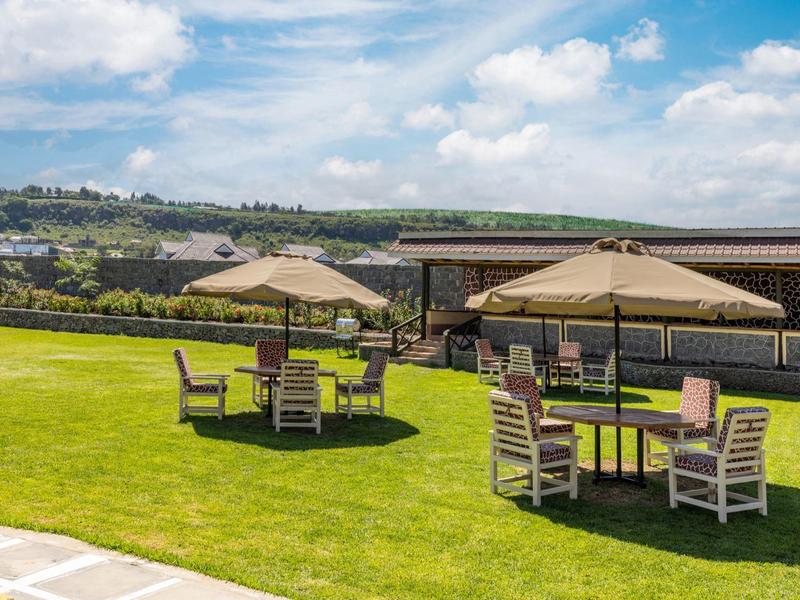 Green lawn with four seating areas and large umbrellas under a blue sky.