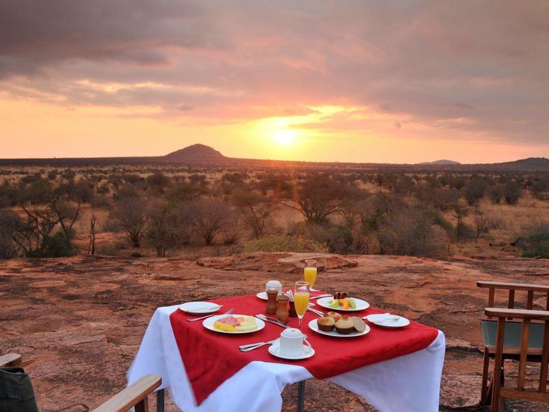 A set table with red cloth and dishes overlooking a landscape at sunset.