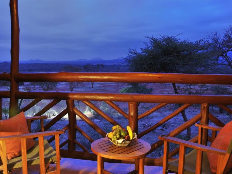 Balcony with wooden railing, two wooden chairs, and table with fruit basket at dusk.