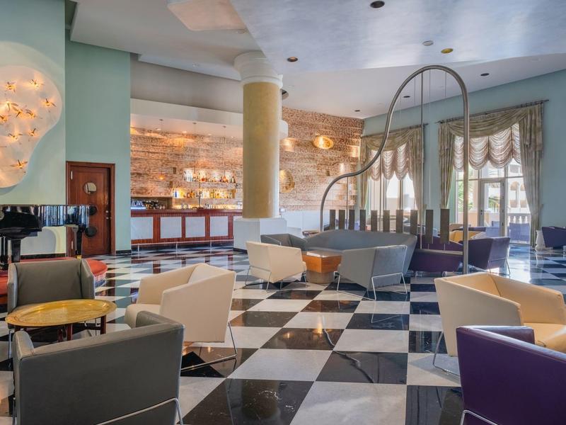 Área moderna del vestíbulo del hotel con asientos coloridos y suelo de ajedrez en blanco y negro.