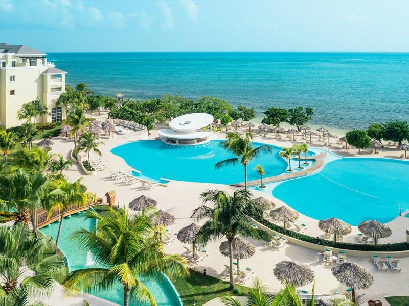 Hotel pool area with multiple pools, palm trees, and ocean view under clear sky