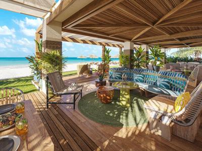 Überdachte Terrasse mit gemütlichen Sitzmöbeln und Blick auf tropischen Strand und Meer.