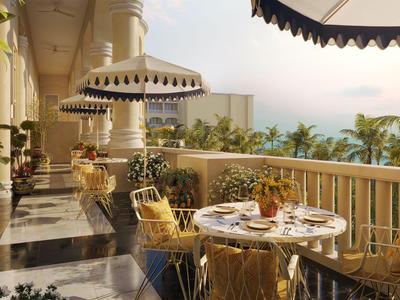 Balkon mit Essbereich, sonnenschirm und Blick auf Palmen und Meer bei klarem Himmel.