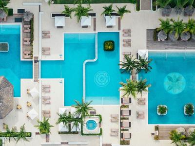 Vogelperspektive auf einen modernen Hotelpool mit Liegestühlen und Palmen.
