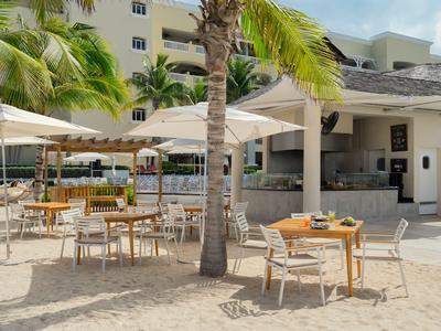 Außenbereich eines Hotels mit Tischen und Stühlen unter Sonnenschirmen am Strand.