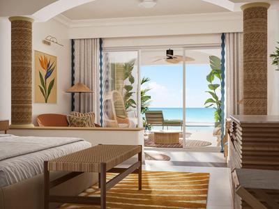 Helles Hotelzimmer mit Doppelbett, Holzbank, Teppich und Meerblick durch große Fenster.