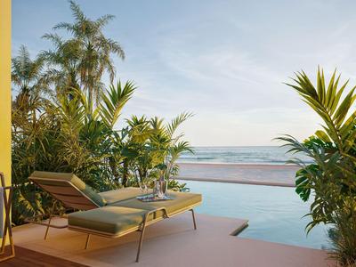 Poolterrasse mit Liegestühl, tropischen Pflanzen und Blick aufs Meer bei klarem Himmel.