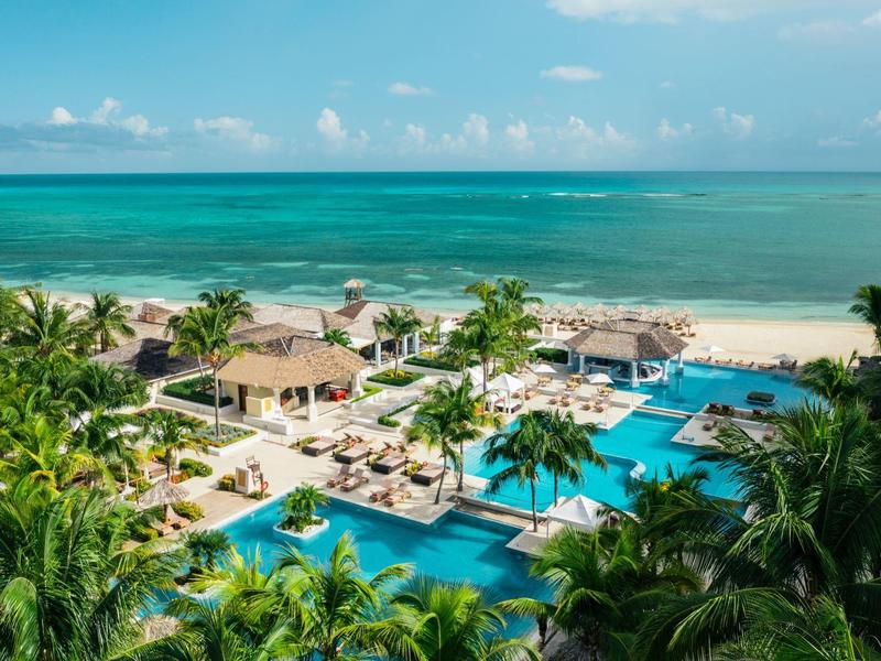 Luxusní bazény v resortu s palmami na pláži s výhledem na modré moře.