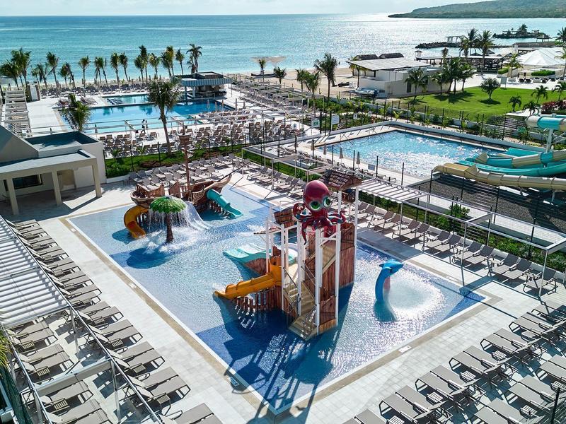 Großer Wasserpark mit Rutschen, Pools, Palmen und zahlreichen Liegestühlen am Meerufer.