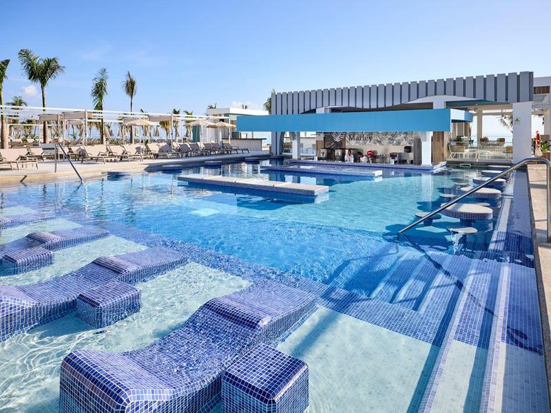 Moderner Außenpool mit blauen Liegen und Barbereich unter strahlend blauem Himmel.