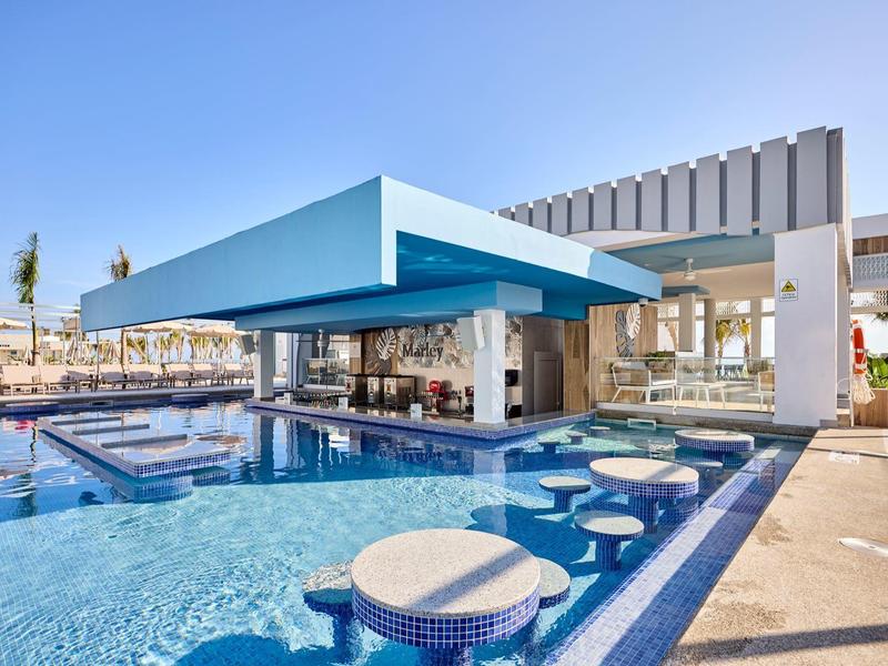 Moderne Bar im Pool mit blauen Sonnendach, runden Sitzgelegenheiten und klarem Wasser bei Tageslicht.