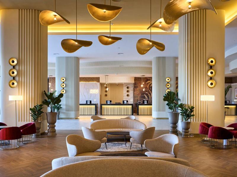 Großer, eleganter Hotel-Lobbybereich mit goldenen Hängeleuchten, bequemen Sesseln und Holzfußboden.