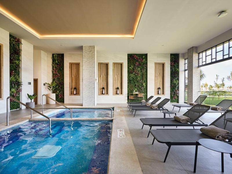 Moderner Innenpool mit blauem Wasser, Liegestühlen und grüner Wanddeko, große Fenster mit Aussicht.