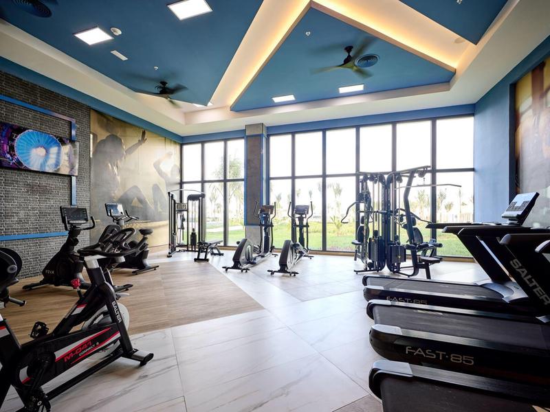 Großer Fitnessraum mit Laufbändern, Fahrrädern und großen Fenstern, helle moderne Einrichtung.