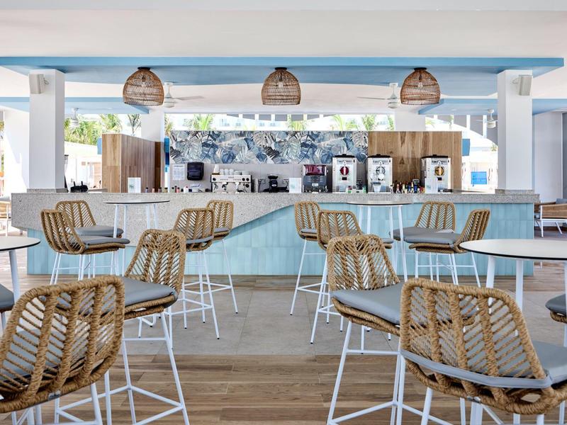 Modernes Café mit hellblauen Tischen, geflochtenen Stühlen und Holzfußboden, offen und lichtdurchflutet.