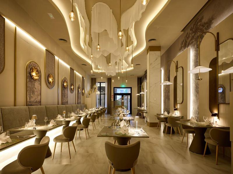 Eleganter, heller Restaurantraum mit modernen Stühlen, Tischen und geschwungenen Deckenleuchten.