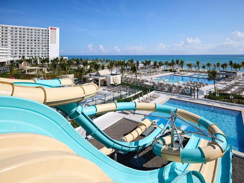 Wasserpark mit großen blauen und gelben Wasserrutschen, Pool, Palmen und Hotel im Hintergrund.