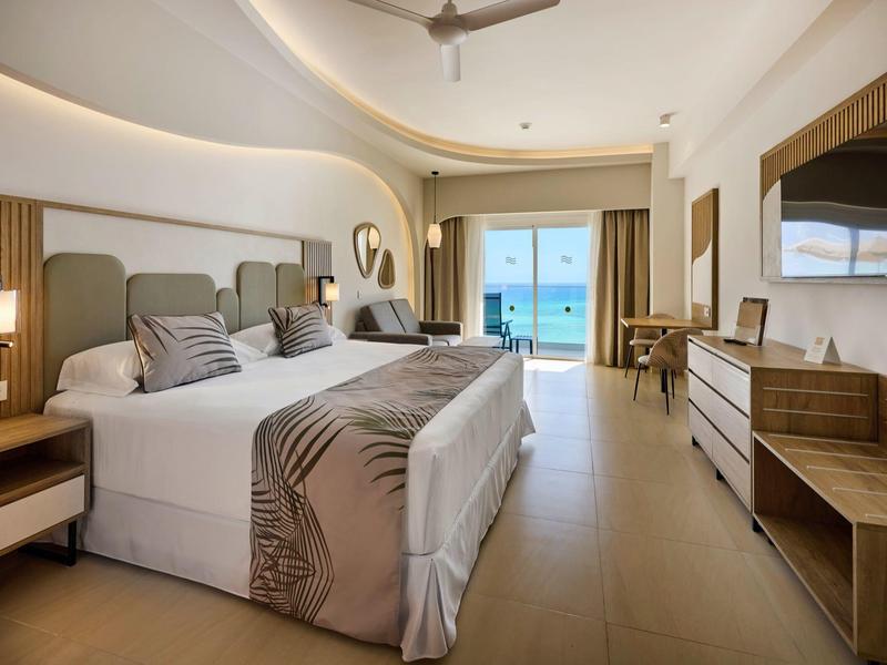 Helles, modernes Hotelzimmer mit großem Bett, Holzmöbeln und Balkon mit Meerblick.