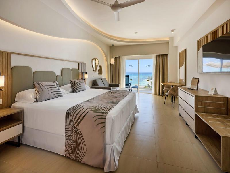 Modernes Hotelzimmer mit Doppelbett, großem Fenster, Balkon und Holz-Möbeln in hellen Farben.