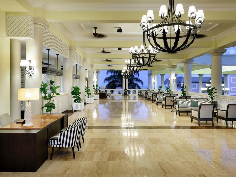 Área moderna del lobby del hotel con suelo de madera, plantas y candelabros con luz cálida.
